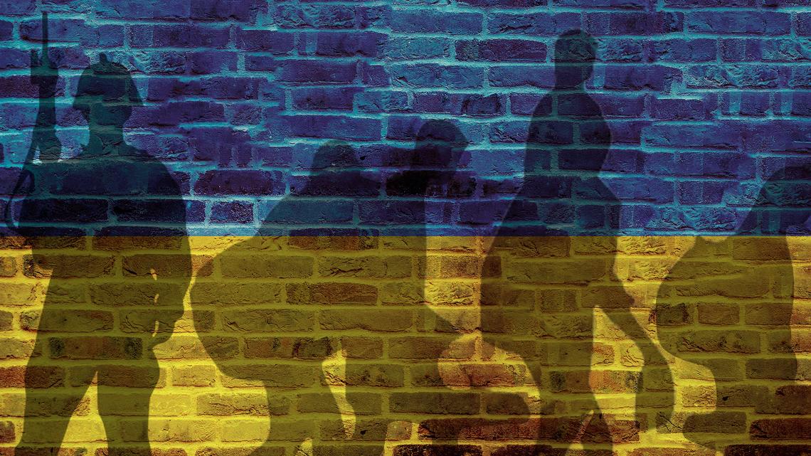 Eine Backsteinmauer, die in den Farben der Ukraine bemalt ist. Oben blau, unten gelb. Darauf sind Schatten von Menschen auf der Flucht und einem Soldat zu sehen.