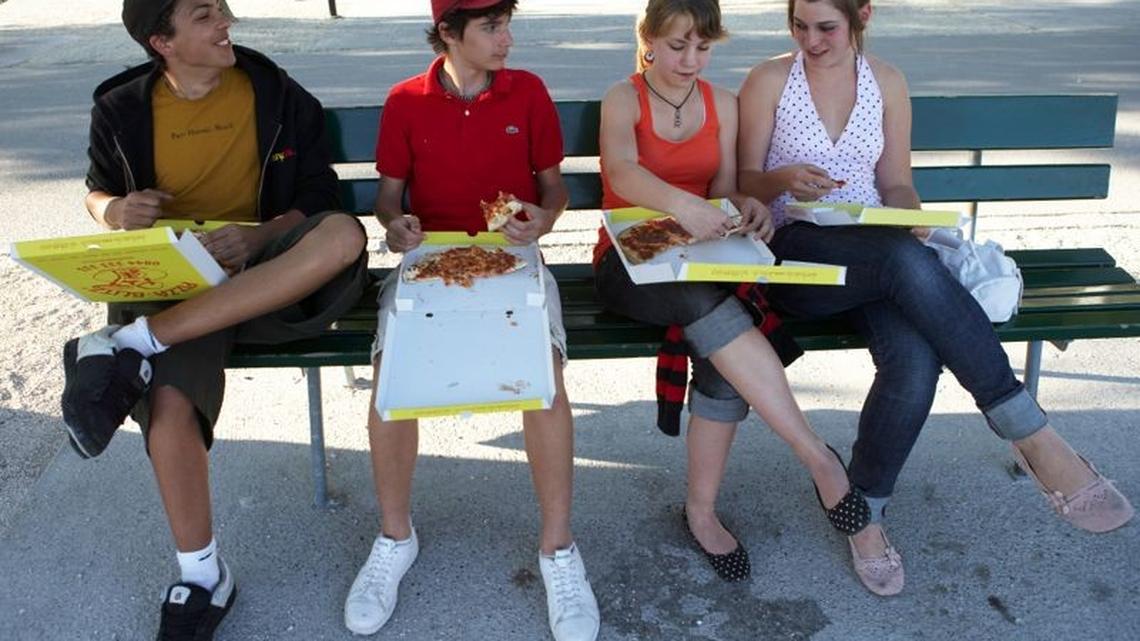 Vier Jugendliche sitzen auf einer Parkbank und essen zu Mittag.