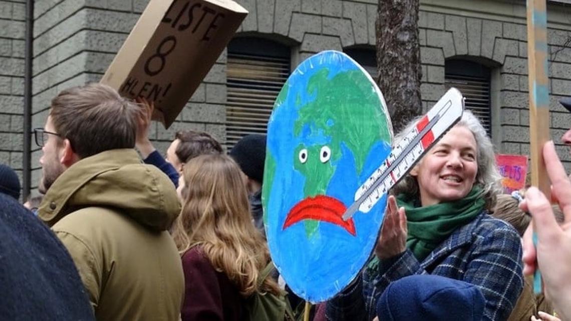 Bild einer Demonstration in Luzern zum Klimastreik. Zwischen Jugendlichen ist ein Plakat sichtbar einer Weltkugel mit traurigem Smilie und Termometer im Mund.