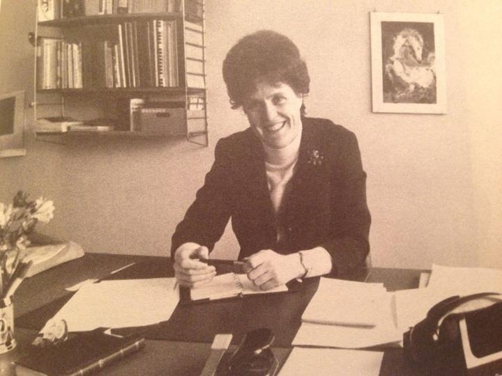 Eine Frau mit kurzen Haaren und einem Blazer an einem Schreibtisch 1971. Es ist ein leicht vergilbtes Schwarz-Seiss-Foto.