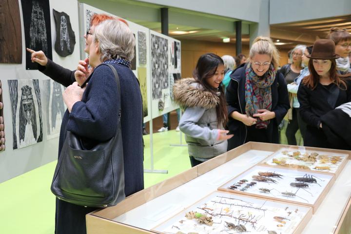 <p>Entwurfsarbeiten und präparierte Insekten werden von Besucherinnen an der Ausstellungseröffnung bestaunt.</p>