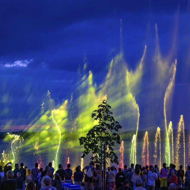 Beleuchtete Wasserfontänen schiessen aus dem Zugersee. Davor steht eine Menschenmenge, die das Spektakel beobachtet.